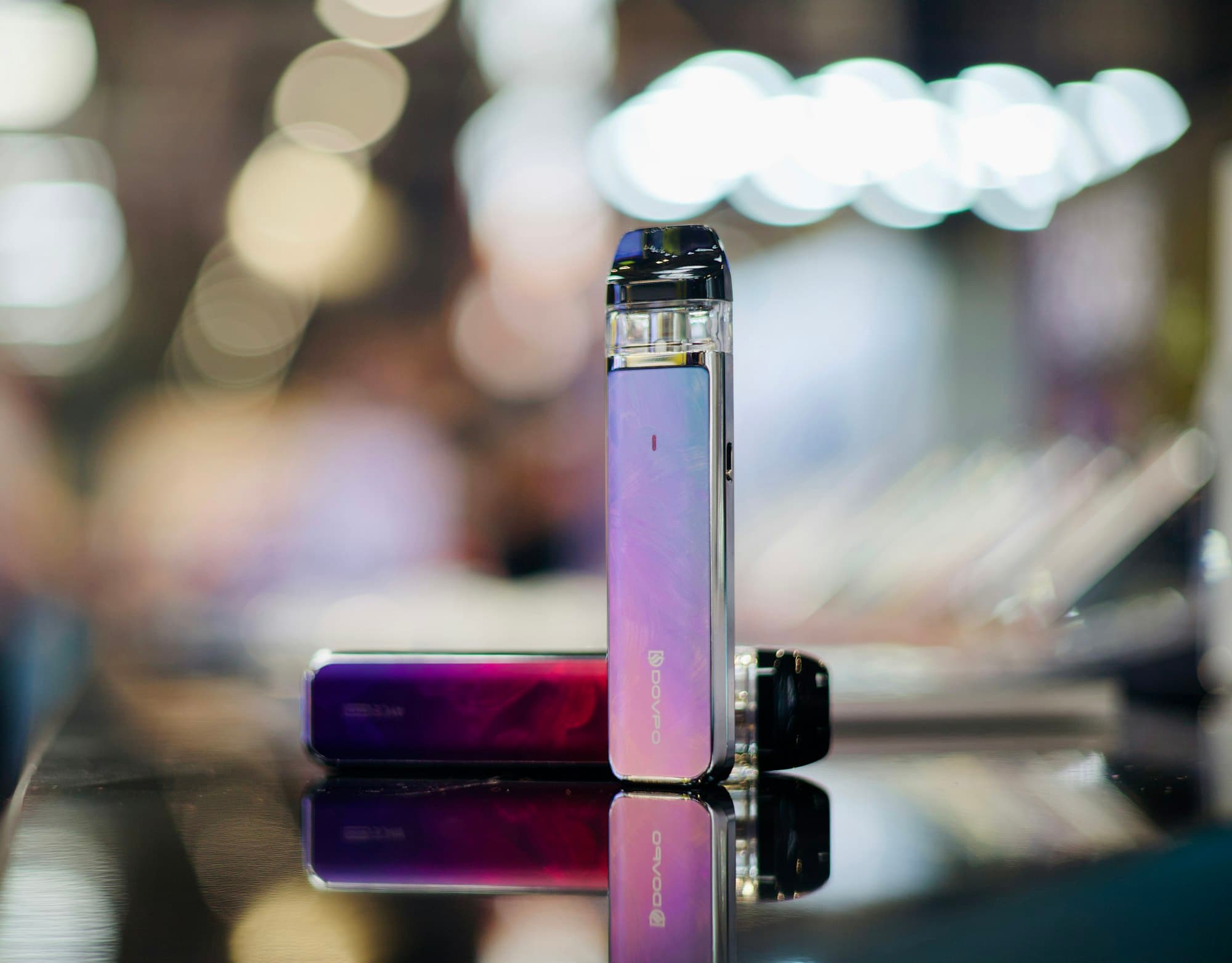 Two rechargeable pod vape kits with replaceable pods standing close together on a table